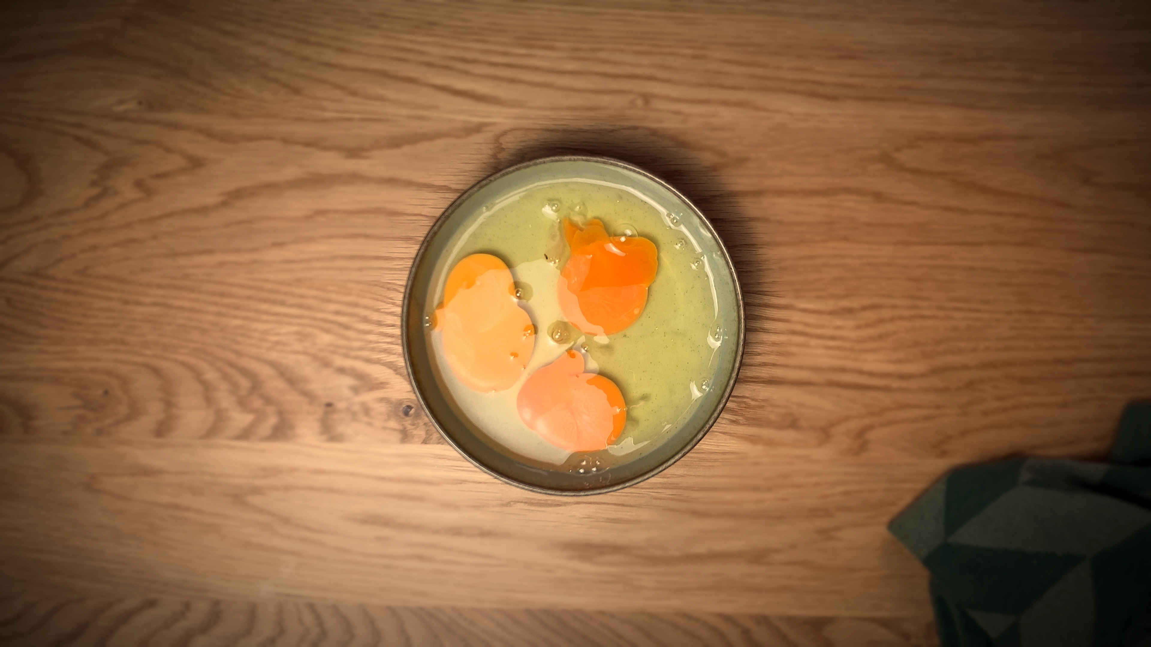 Top-down view of three raw eggs inside a sage green porcelain bowl.