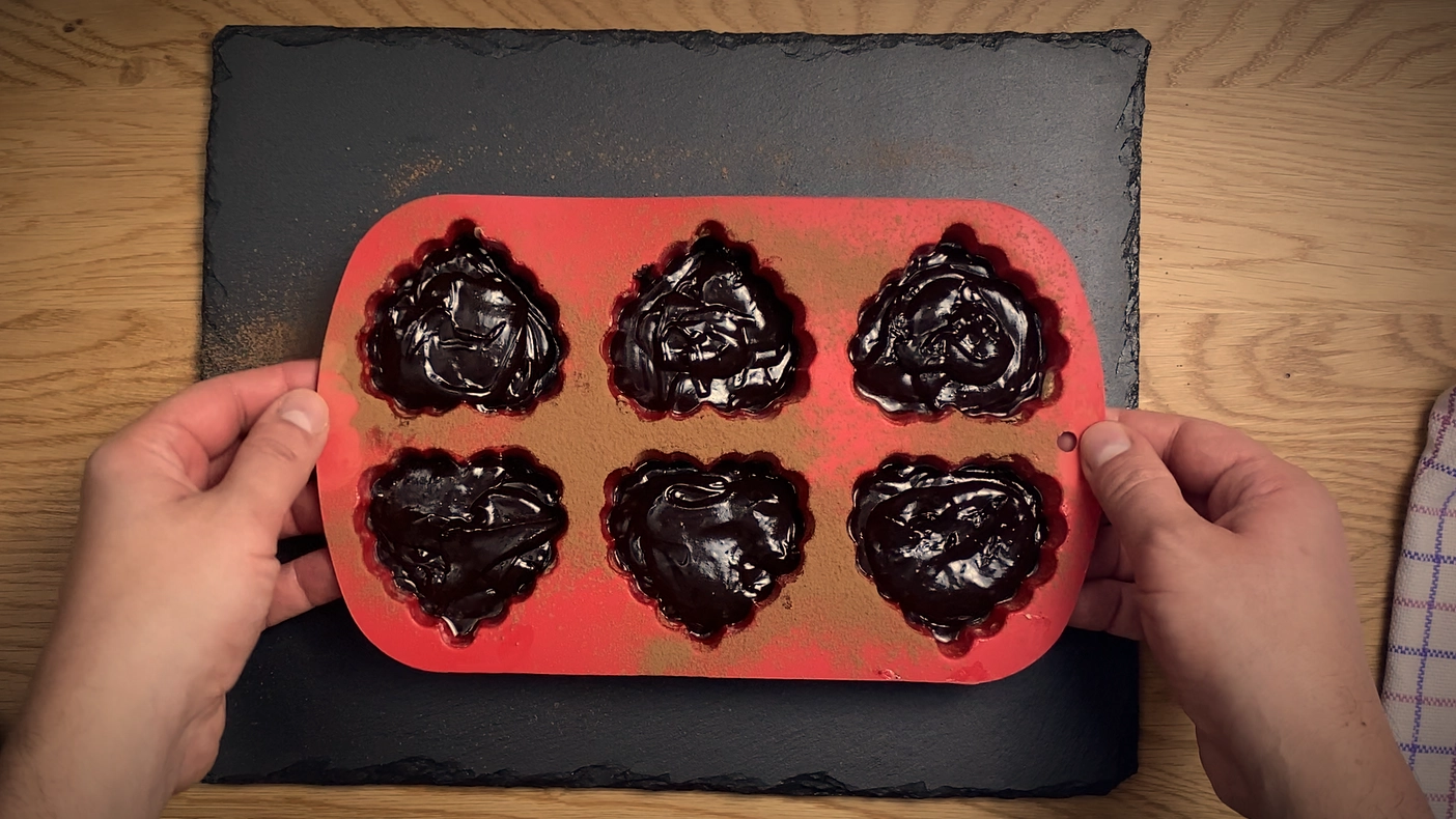 Brownie batter spooned into six heart-shaped silicone molds before baking.